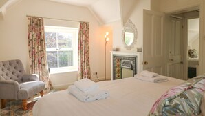A bedroom with a large bed, a chair, a fireplace, and a window with curtains. - Holmefield (Bakewell)