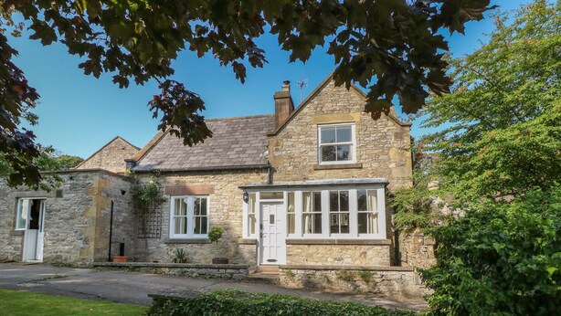 A stone house with a white door, a window with curtains, and a small garden area. - Holmefield (Bakewell)