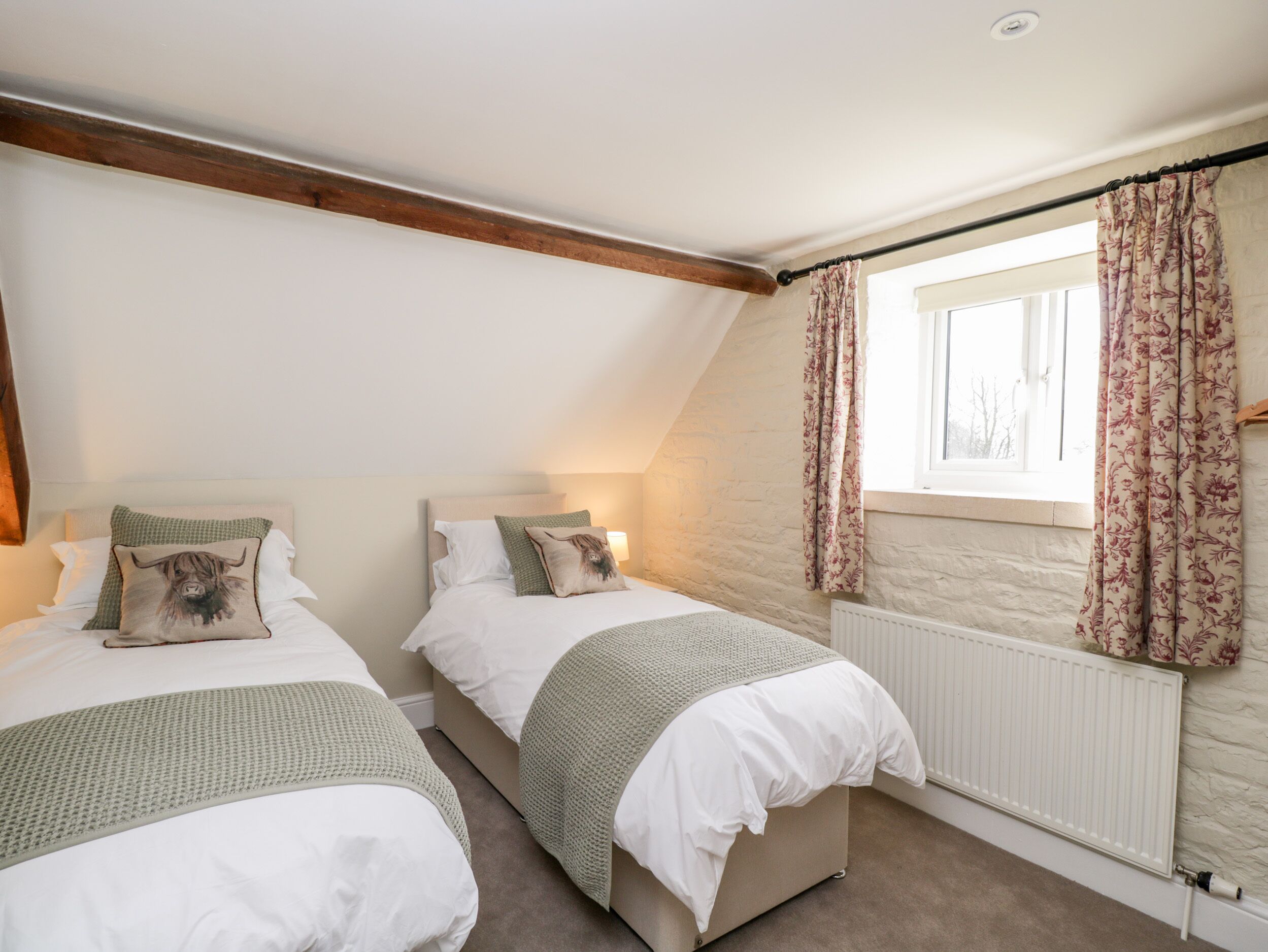 A bedroom with two beds, a window with floral curtains, and a stone wall.