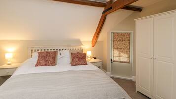 A bedroom with a large bed, wooden beams, a wardrobe, and a door with patterned curtains.