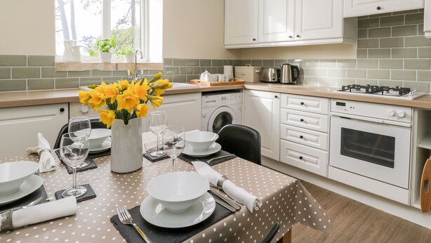 Une cuisine moderne avec des meubles blancs, un coin repas agrémenté d’une nappe à pois et une fenêtre donnant sur la verdure.