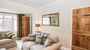Un salon avec un canapé beige, deux fauteuils, une armoire en bois et un miroir au mur.