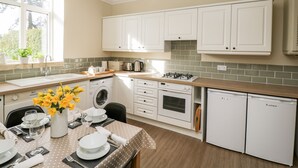 Une cuisine moderne avec des armoires blanches, un four encastré, un lave-vaisselle et un coin repas avec une table dressée pour deux personnes.