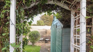 A covered patio area with a table and chairs, a small bush, and a green shed. - Y Bwthyn, Newport (Newport)