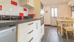 A modern kitchen with white cabinets, red accents, a black countertop, and a dining area with wooden chairs and a table. - Y Bwthyn, Newport (Newport)