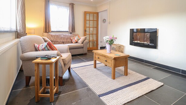 A modern living room with a sofa, armchairs, a coffee table, and a TV mounted on the wall. - Y Bwthyn, Newport (Newport)