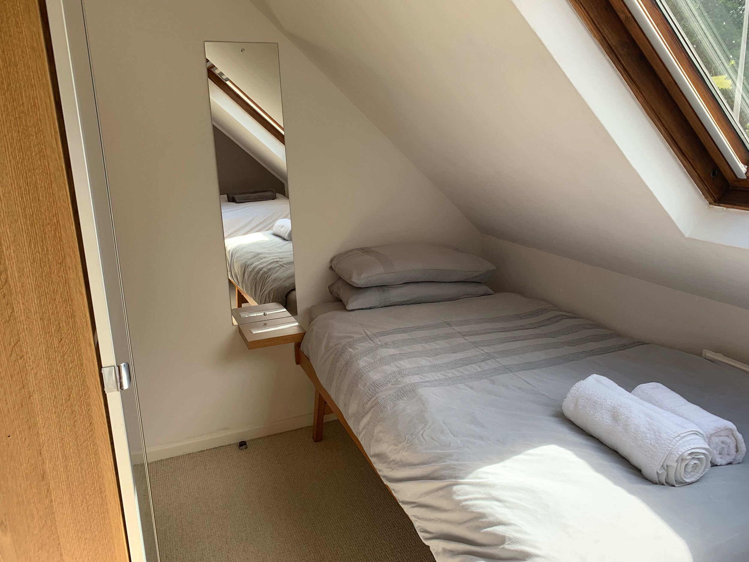 A small, sloped room with a single bed, a nightstand, and a window.