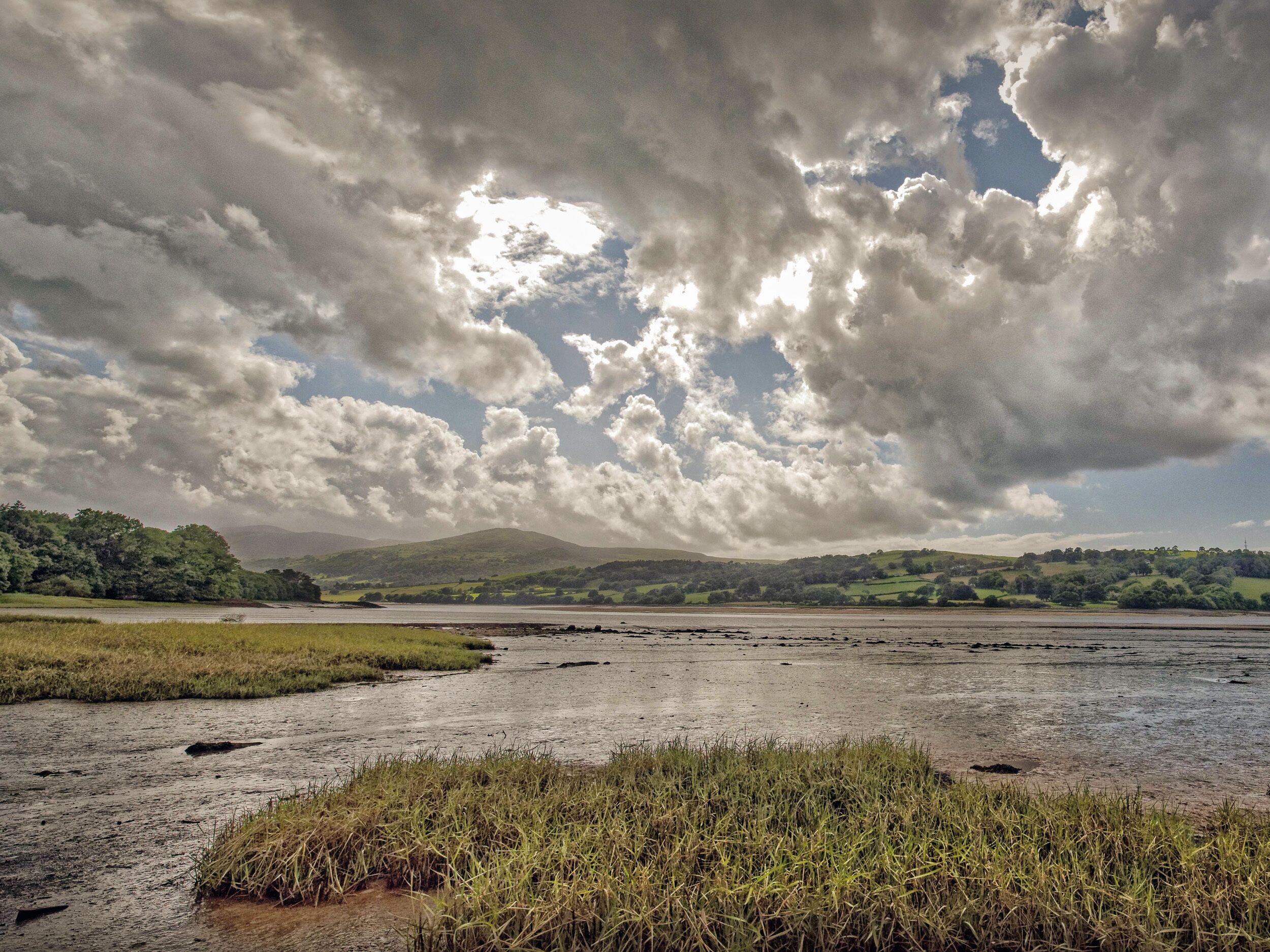A landscape with a river, grassy areas, and hills in the background.