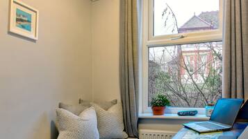 Una habitación acogedora con una cama, un ventanal con vistas a edificios, un escritorio con una computadora portátil y una planta en maceta.