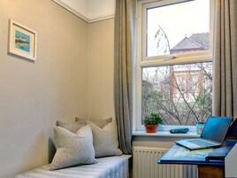 Una habitación acogedora con una cama, un ventanal con vistas a edificios, un escritorio con una computadora portátil y una planta en maceta.