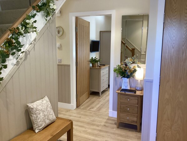 A hallway with a wooden bench, a small table with a lamp, and a mirror reflecting the room.