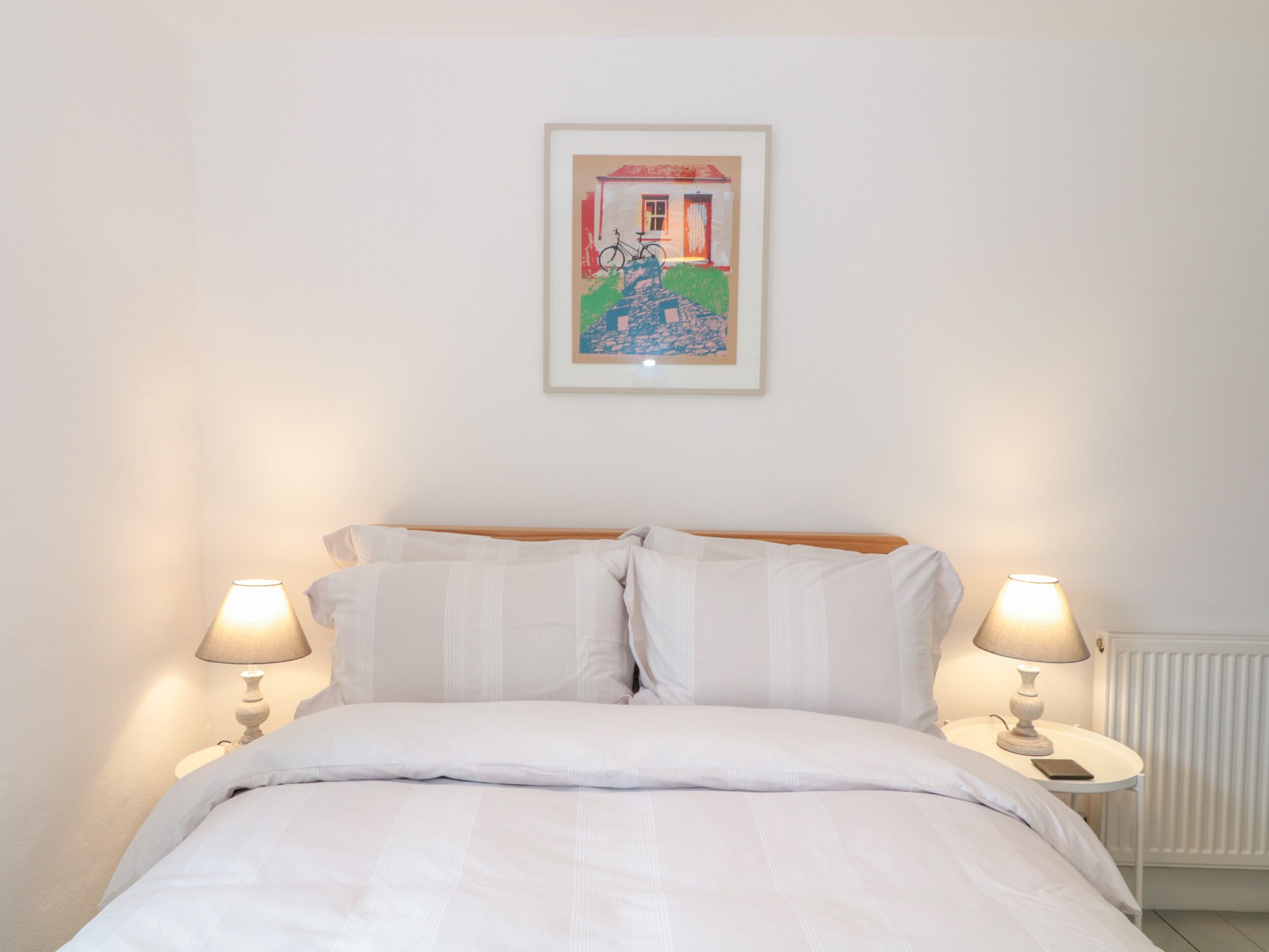 A neatly made bed with white bedding, two bedside lamps, and a framed picture on the wall.
