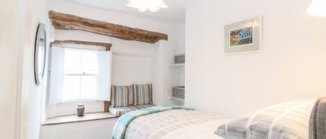 Un dormitorio con ventana, una cama con ropa de cama a rayas, una lámpara colgante y un cuadro en la pared.