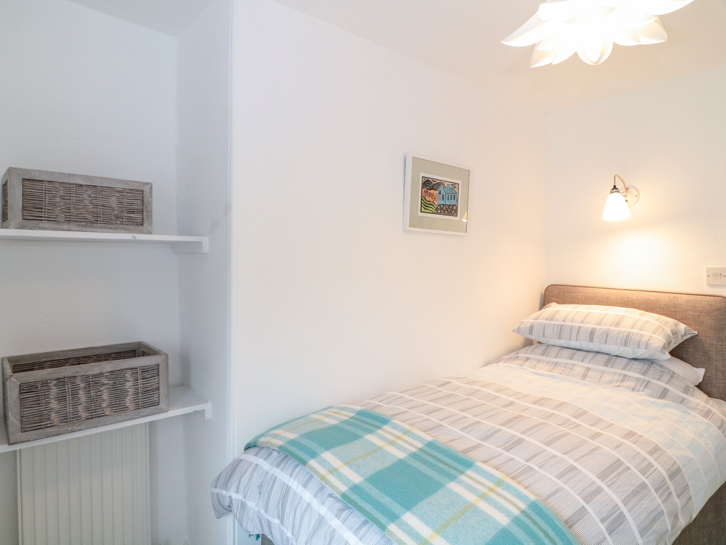 Un dormitorio con cama, estante en la pared, un cuadro enmarcado y lámpara de pared.