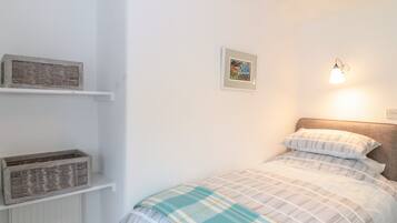 Un dormitorio con cama, estante en la pared, un cuadro enmarcado y lámpara de pared.