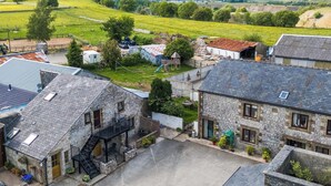 Un village rural avec des bâtiments en pierre, une cour pavée et une vue sur des collines verdoyantes à l’horizon.