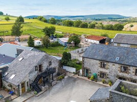Un borgo rurale con edifici in pietra, un cortile pavimentato e vista su dolci colline in lontananza.