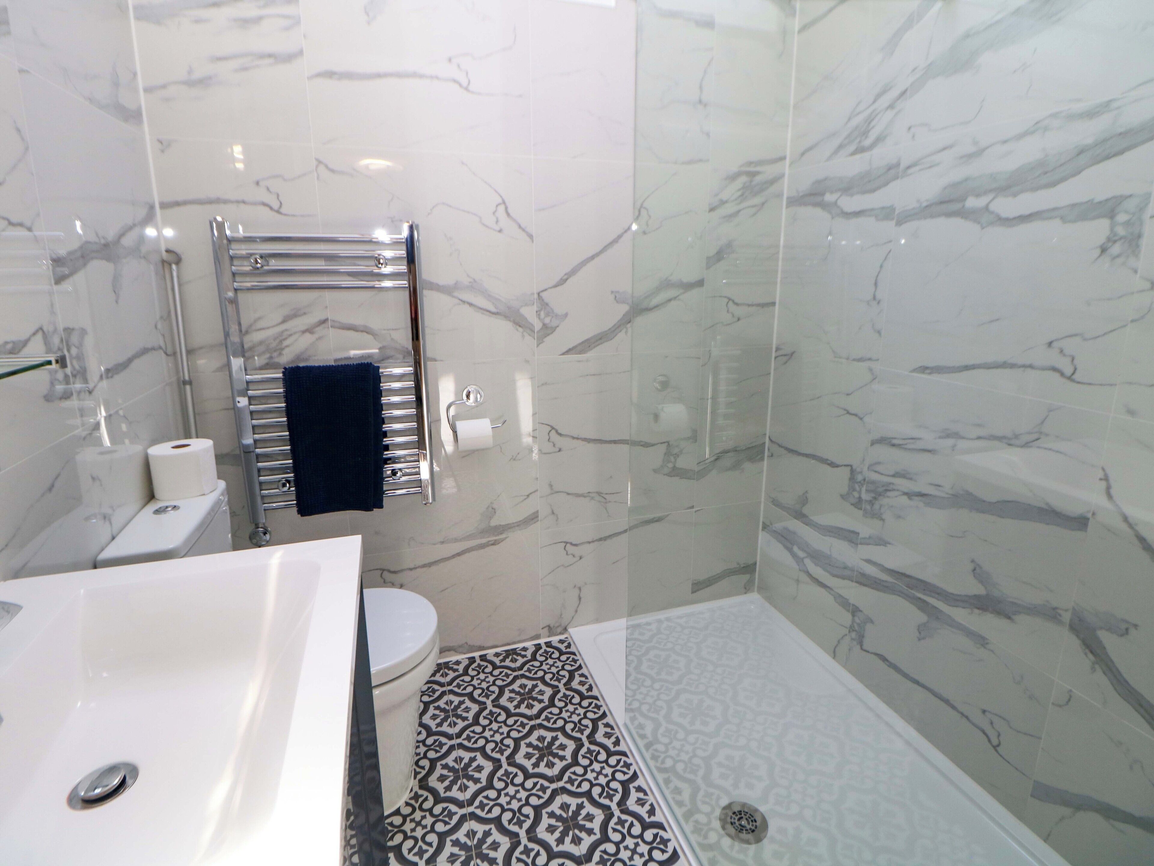 A bathroom with a white bathtub, a toilet, and a shower area with patterned tiles.