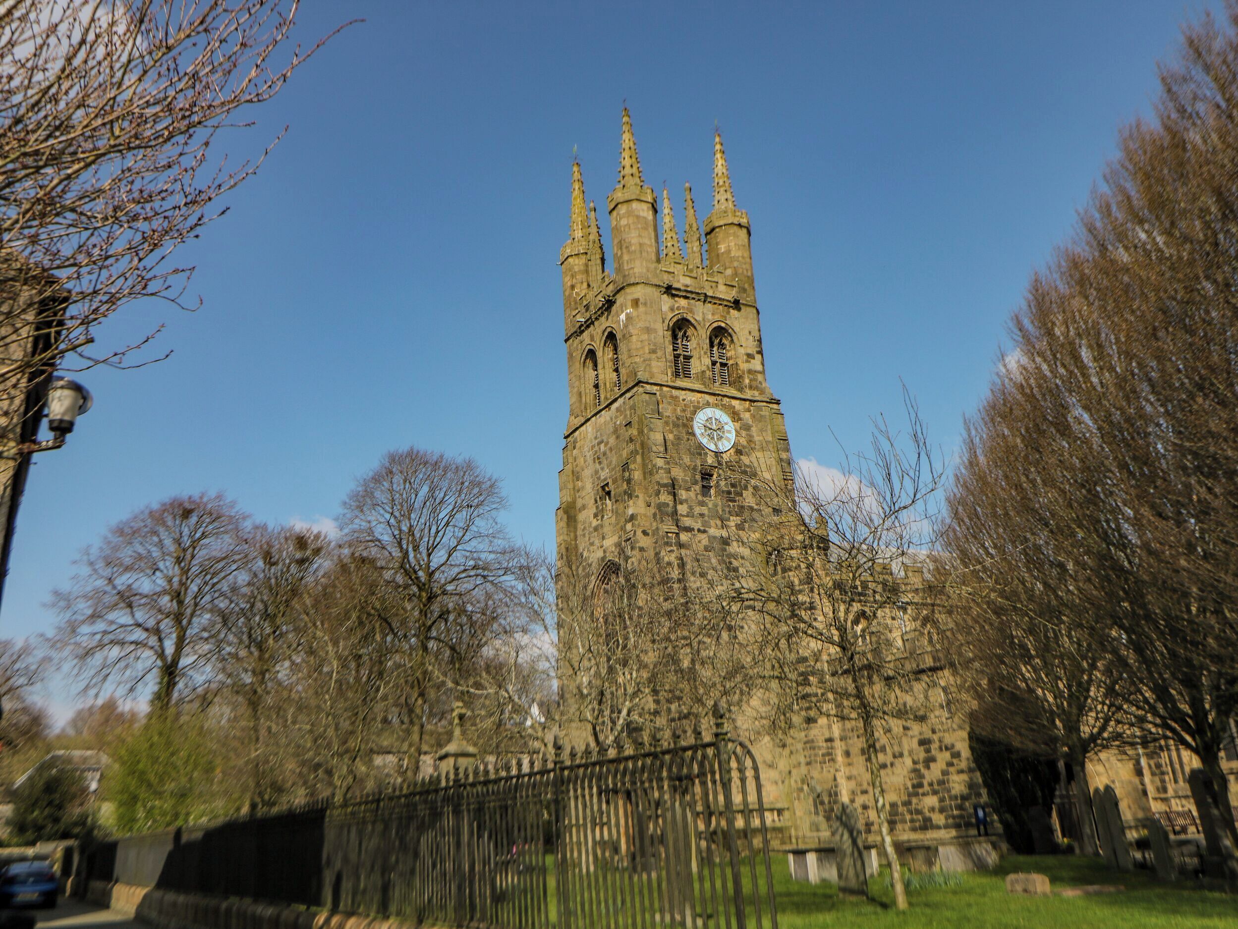 A historic stone tower with a clock, surrounded by trees and a fence.