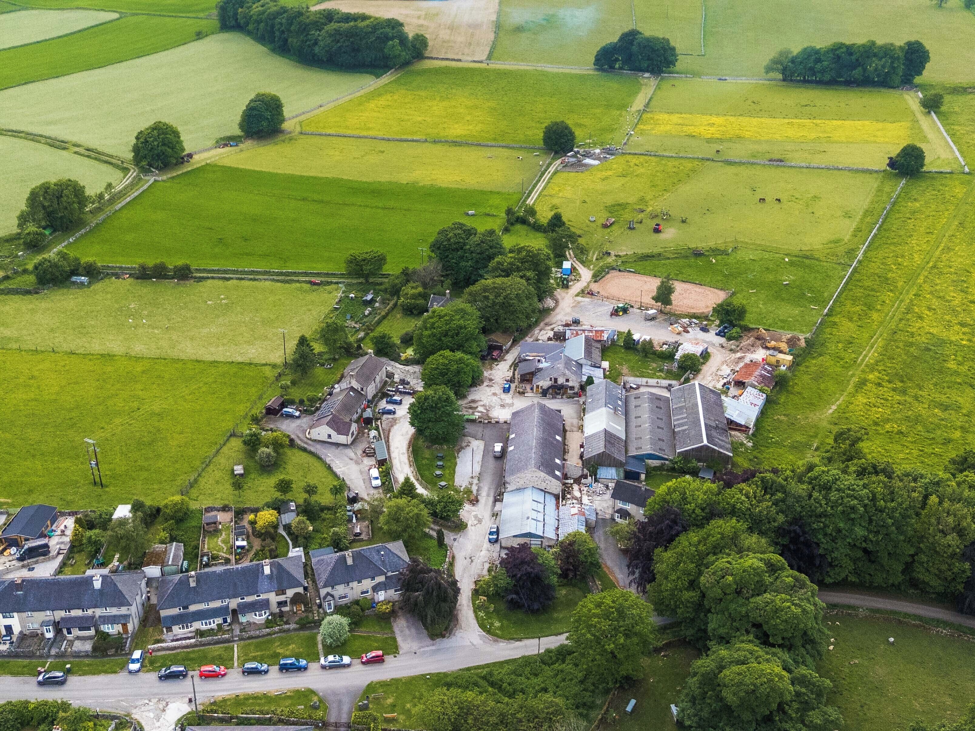 An aerial view of a rural area with fields, a small cluster of buildings, and a road.