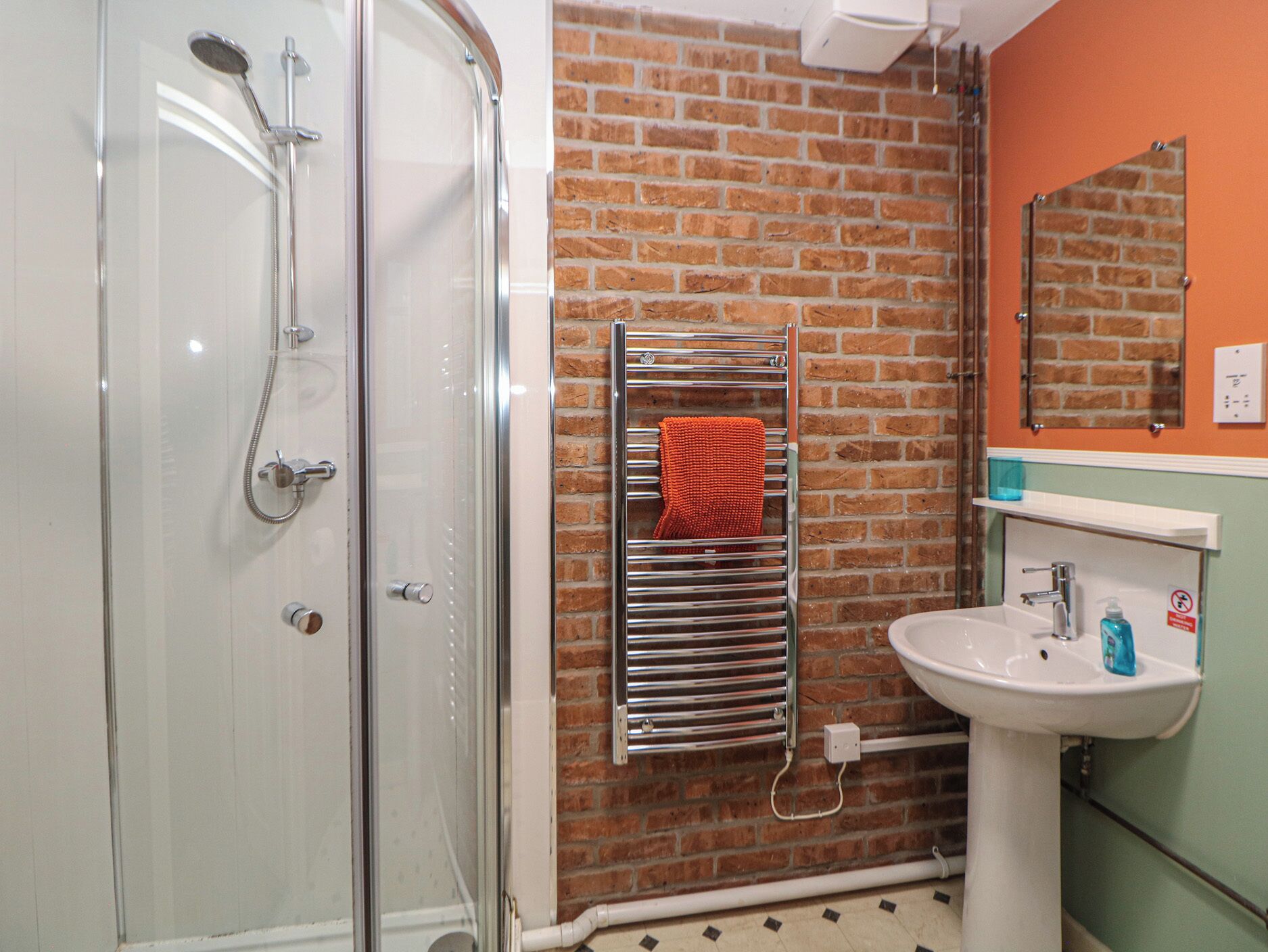 A bathroom with a glass shower enclosure, a towel rack with an orange towel, a sink, and a mirror.