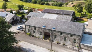 Un bâtiment en pierre avec un toit en pente, une allée pavée et un petit espace de stationnement.