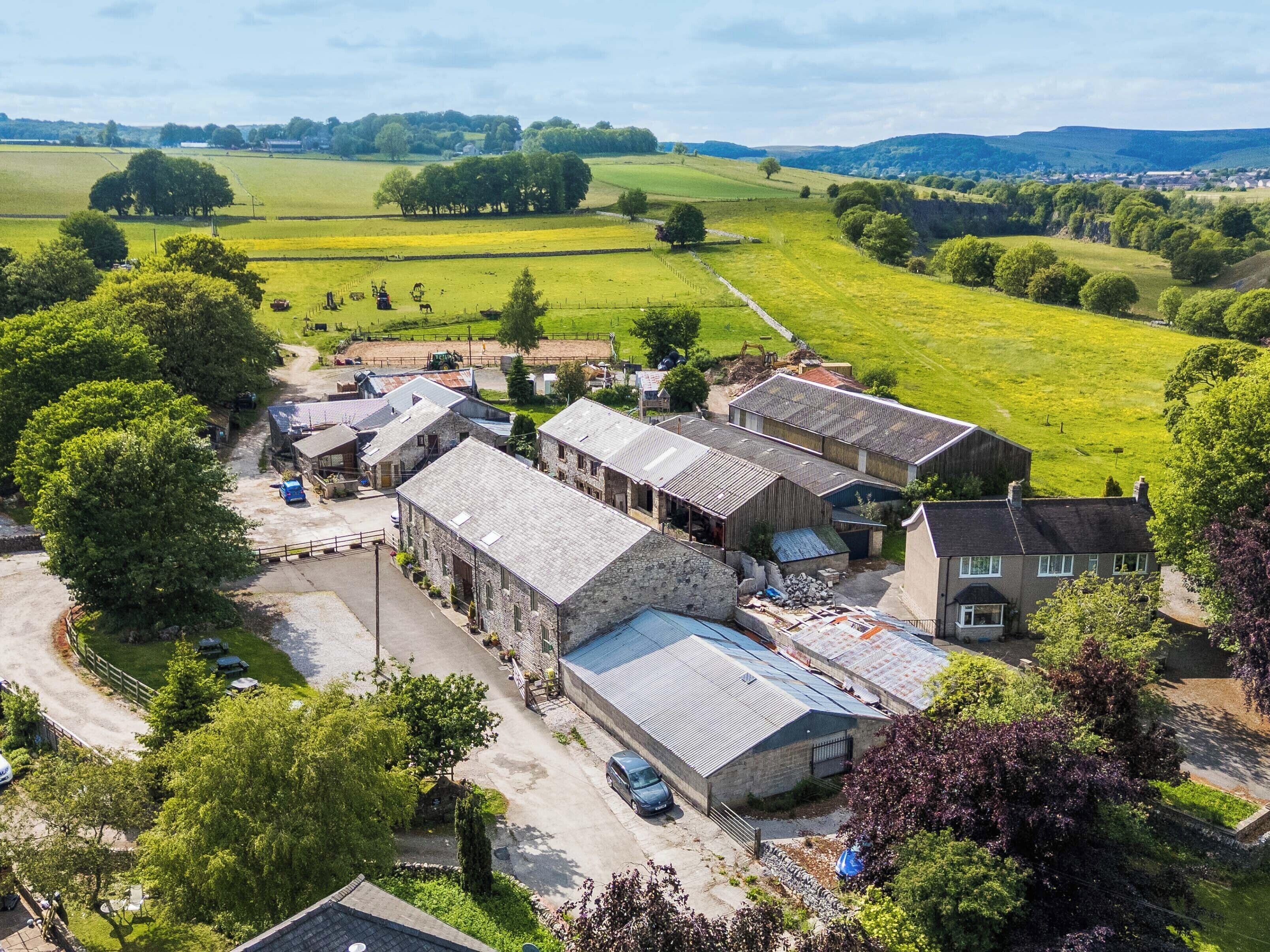 A rural property with stone buildings, a paved driveway, and surrounding green fields.