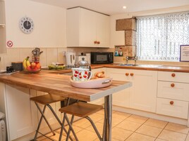 Una cucina moderna con mobili bianchi, un piano di lavoro in legno, un lavello, un forno a microonde e una sveglia appesa al muro.