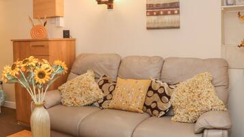 A living room with a beige sofa, decorative pillows, a vase with sunflowers, a wooden cabinet, and a wall-mounted light fixture.