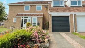 A two-story residential building with a tiled roof, a garage, and a front garden with various plants. - Teàrlach House (Alnwick)
