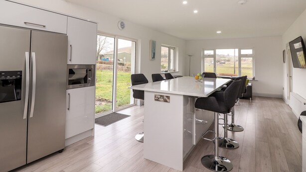 A modern kitchen with a central island, stainless steel appliances, and large windows offering a view of the outdoors. - Coolnaharragill Lower (Glenbeigh)