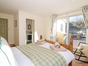 A bedroom with a bed, a wooden headboard, a green plaid blanket, and a view of an outdoor patio with a table and chairs. - Giggling Goose Cottage (Woodhall Spa)