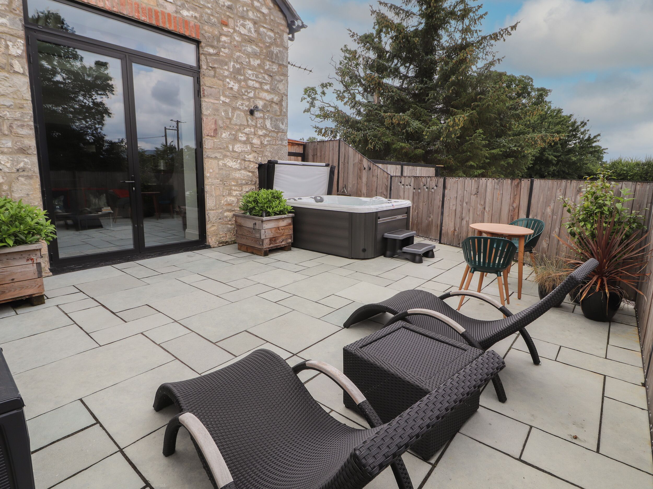 A patio with wicker lounge chairs, a hot tub, and a wooden table.