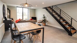 A modern kitchen with a wooden dining table, black chairs, and a staircase with black railings. - The Old Workshop (Denbigh)