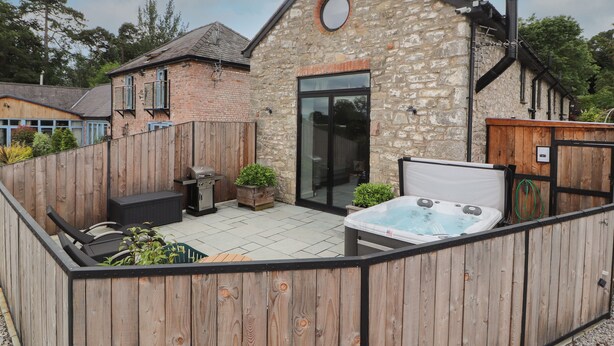 A stone building with a wooden deck, a hot tub, and a barbecue grill. - The Old Workshop (Denbigh)