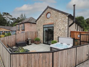 A stone building with a wooden deck, a hot tub, and a barbecue grill. - The Old Workshop (Denbigh)
