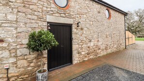 A stone building with a black door and two circular windows. - The Old Workshop (Denbigh)