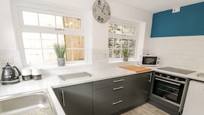 A modern kitchen with a sink, stove, microwave, and two windows.