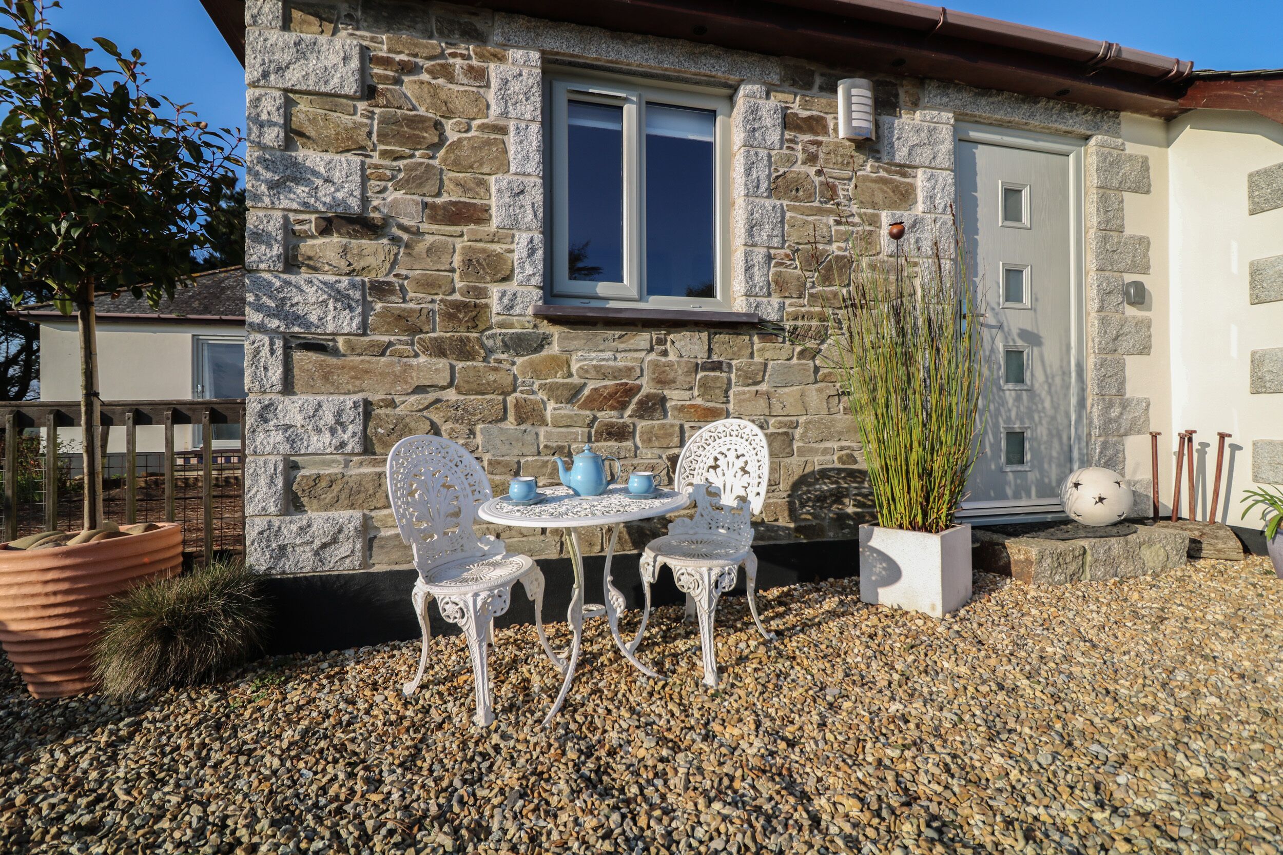 A stone house with a small patio area featuring a table and chairs, a potted plant, and a decorative sphere.
