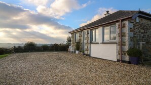 A stone house with a gravel driveway, a wooden fence, and a view of the countryside. - Valley View (St Austell)