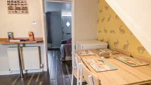 A room with a wooden dining table, chairs, a radiator, a white cabinet, and a wall with a rabbit pattern. - Scarborough Cottage (Driffield)