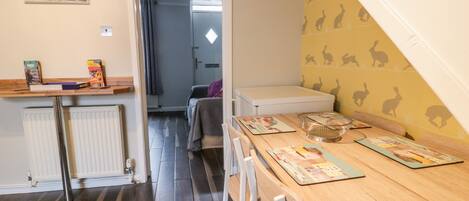 A room with a wooden dining table, chairs, a radiator, a white cabinet, and a wall with a rabbit pattern.