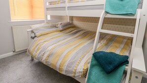 A bunk bed with a striped bedspread, a window with blinds, and a radiator. - Scarborough Cottage (Driffield)