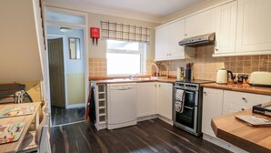 A modern kitchen with white cabinets, a built-in oven, and a window with blinds. - Scarborough Cottage (Driffield)