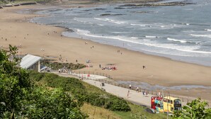 Uma praia com um calçadão pavimentado, uma torre salva-vidas e uma vista distante de uma cidade.