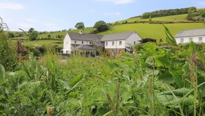 A white house with a grey roof, surrounded by lush green fields and hills. - Llety Ceiro (Bow Street)