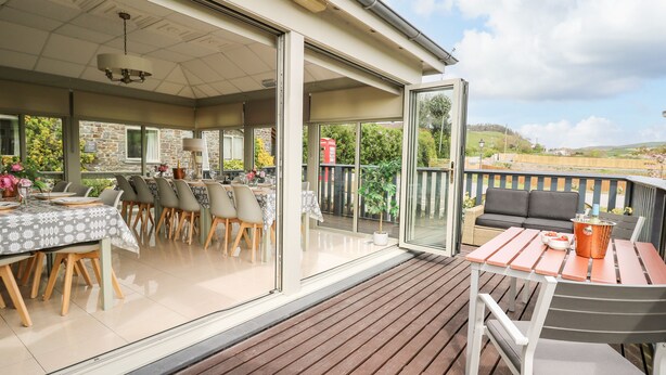 An outdoor dining area with a table set for four, a wooden deck, and a view of the countryside. - Llety Ceiro (Bow Street)