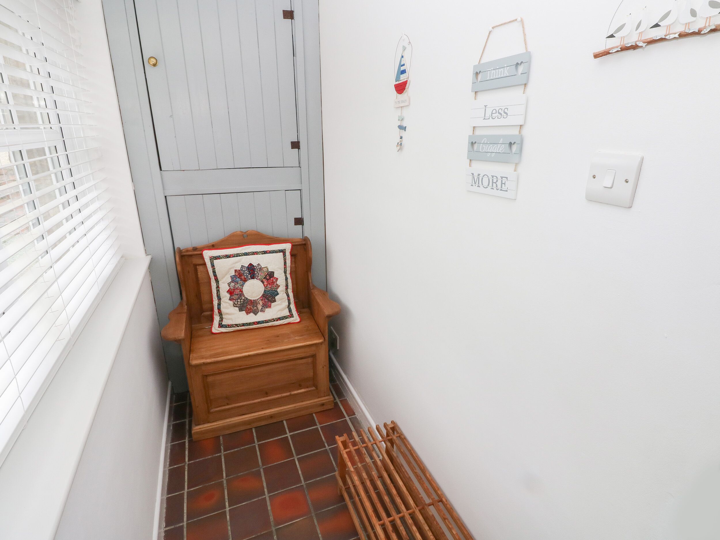 A narrow hallway with a wooden bench, a decorative pillow, a door, and wall-mounted signs.