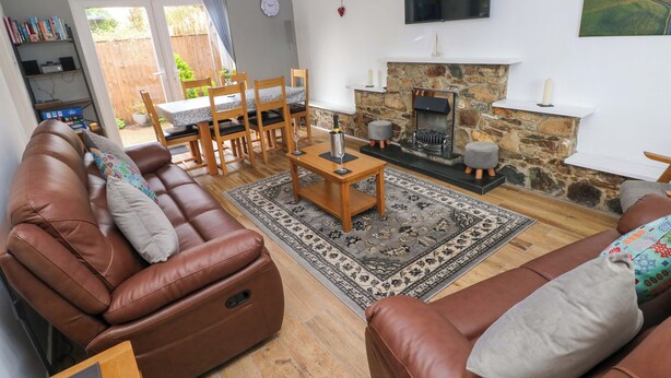 A living room with a sofa, a coffee table, and a fireplace. There is a television mounted on the wall and a bookshelf in the corner. - Ty'r Winllan (Newport)