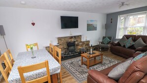 A living room with a fireplace, a sofa, a dining table with chairs, and a television mounted on the wall. - Ty'r Winllan (Newport)